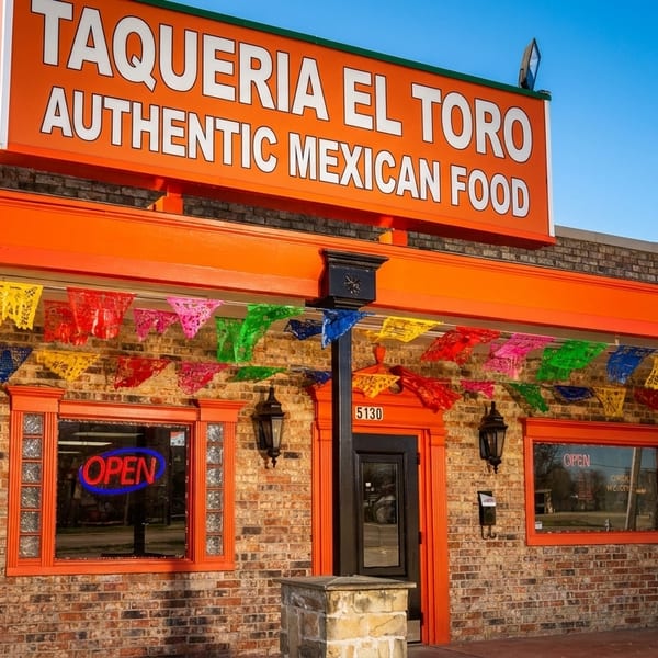 Exterior of Taqueria El Toro, a brick building with an orange sign and colorful papel picado decorations.