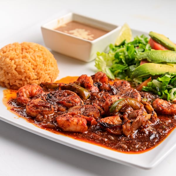 Shrimp in red sauce with rice, refried beans, and a fresh salad with avocado slices.