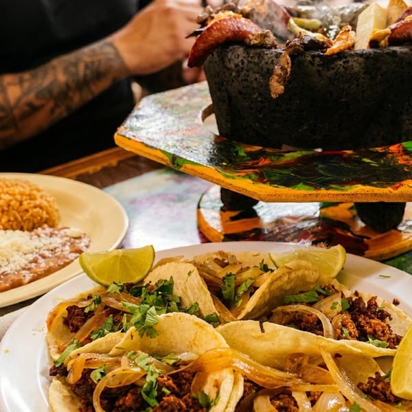A table laden with Mexican food, including tacos, rice, beans, salad, and a molcajete.